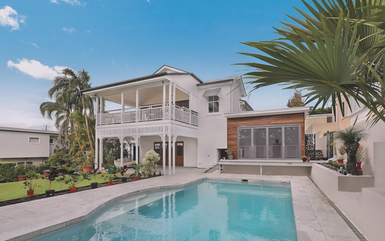 A backyard pool beside a white two-storey house on a clear day