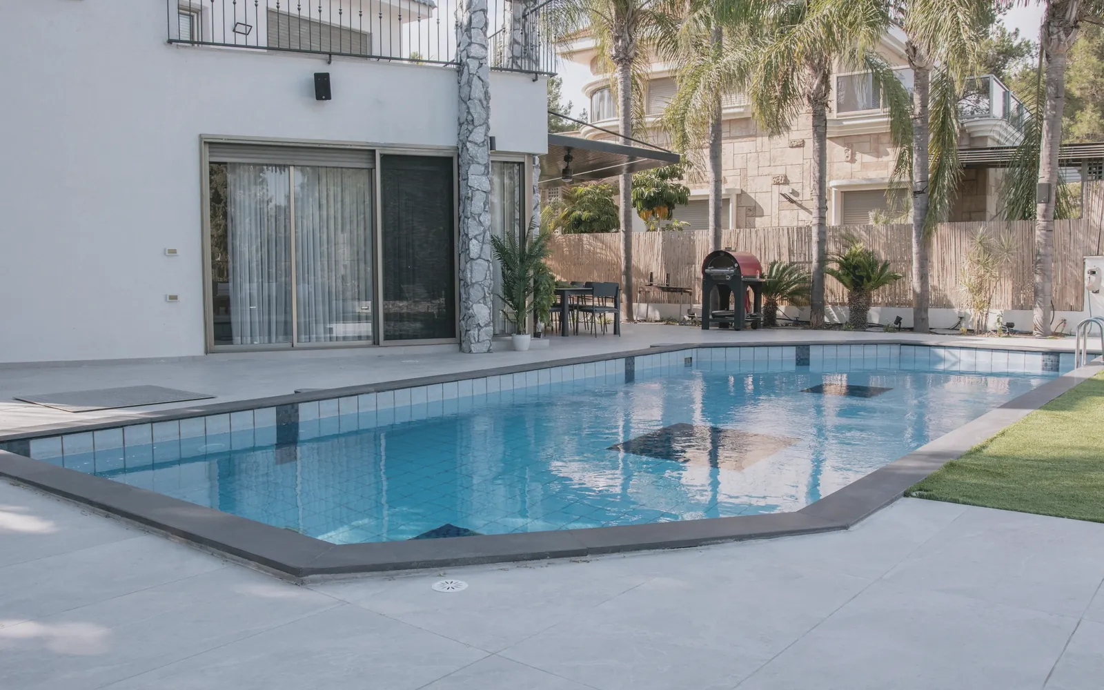 A clean backyard pool with a tiled edge and palm trees
